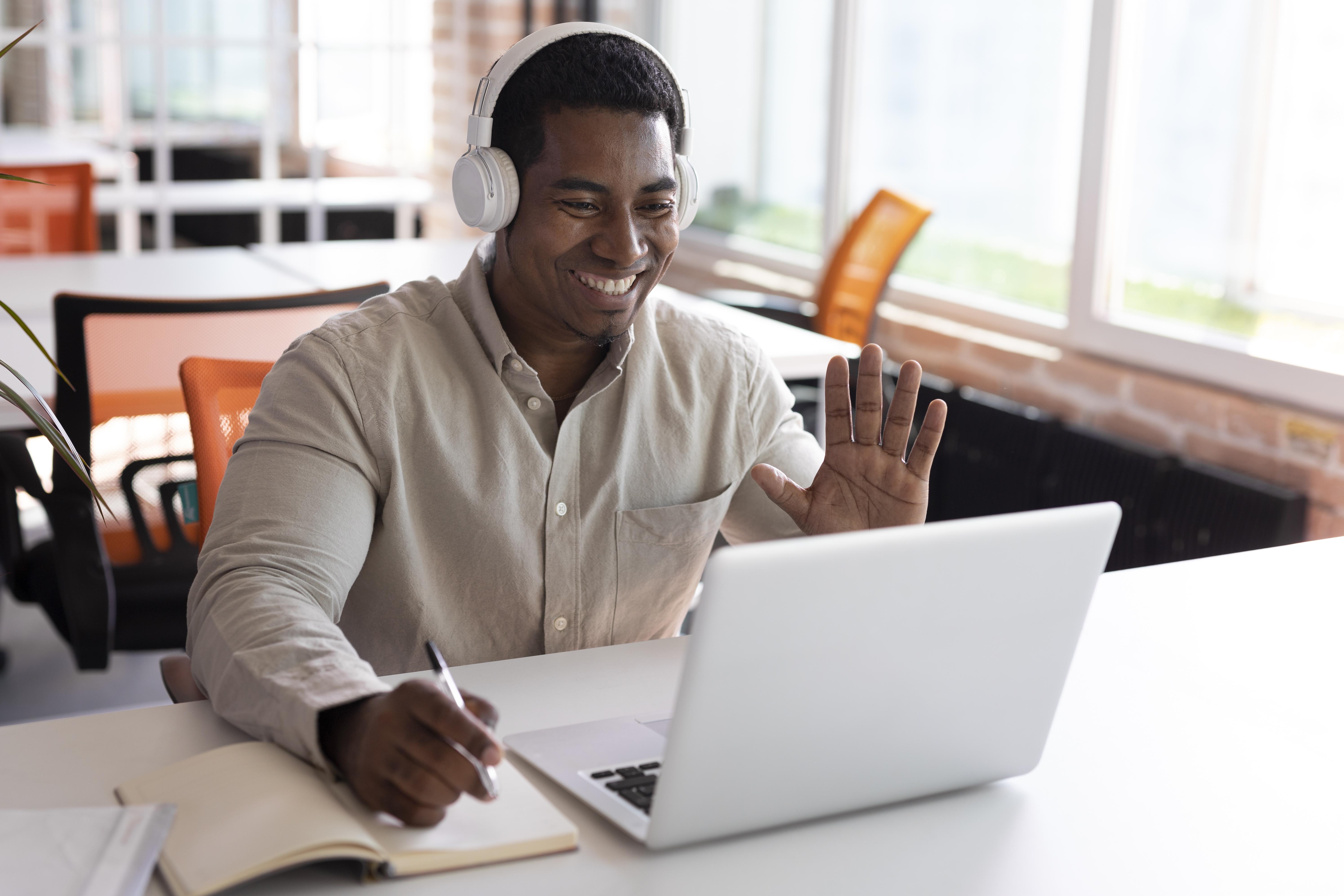 Man working on laptop with friendly wave